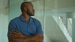 © Krakenimages.com - Young man with crossed arms standing confidently in an office interior, showcasing professionalism and thoughtfulness in a modern workplace setting