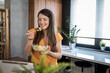 © Migma_Agency - Happy woman eating fresh salad and having video call in kitchen
