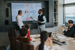 © qunica.com - A diverse group of business people engage in a meeting, discussing strategies and data displayed on a large screen in a modern office setting.