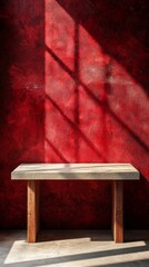 Fototapete - Golden rays filter through a nearby window, casting intricate shadows on a simple wooden table. The deep red wall adds warmth, creating an inviting atmosphere for creativity