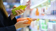 © Pavel - A female customer compares two different shampoo bottles for hair care, reading labels and examining ingredients. Self-care and conscious choice. Close-up of a woman's hands in a cosmetics department