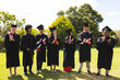 © Wavebreak Media - Graduating diverse students in caps and gowns celebrating success in garden with diplomas