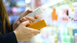 © Pavel - A female customer reading the ingredient labels compares two Skincare or Beauty products. Close-up of a woman's hands in cosmetic store. Makeup selection. Conscious choice. Self-care. Mindful shopping