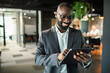 © Marko Geber - Smiling black businessman using tablet in modern office