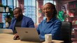 © DC Studio - African american woman checking reports in a notebook to solve tasks with her partner, doing freelance work from the comfort of their home. Focused people doing research with laptop. Camera A.