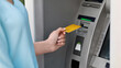 © Prostock-studio - Unrecognizable woman putting gold credit card into ATM outdoors to take money cash, cropped image, closeup