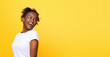 © Prostock-studio - Emotional african american woman looking at empty space over her shoulder, yellow studio background. Young happy black lady with open mouth impressed by great offer, panorama with free space