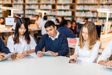 Fototapete - Students studying in a library, using tablets. Diverse group focused on learning. Library setting with books, students, and technology. Educational environment. Diverse students learning at library.