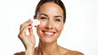 © Netaya - Smiling middle aged mature woman in her 50s applies facial cream on face looks at camera isolated on white background showcasing anti age healthy dry skin care beauty therapy old skincare treatment co