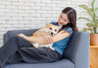 © Bangkok Click Studio - Portrait of asian young beautiful woman happy smile hugging puppy cute welsh corgi dog sitting on sofa playing funny animals in living room, concept embracing lifestyle enjoying trust love pet friend.