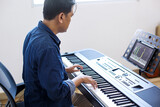 Adult Man Learning To Play Piano Using Digital Tablet With An Online Lesson And Course