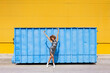 © VISTA by Westend61 - Woman with curly afro hairstyle dancing happily in front of a blue container and yellow wall
