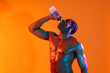 © VISTA by Westend61 - Athlete drinking water during workout in studio with colorful lighting