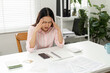 © wichayada - Home Office and Stress Management. A woman deals with the stress of financial paperwork while sitting at her home desk, looking overwhelmed.