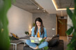 © Migma_Agency - Young woman working from home using laptop on sofa in modern apartment