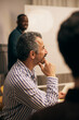 © Maskot - Side view mature male creative professional sitting with hand on chin in meeting room at office