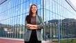 © PeopleVideos - Smiling businesswoman posing with folded arms in front of modern office building