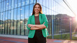 © PeopleVideos - Smiling businesswoman posing with crossed arms in front of modern office building