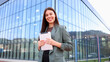 © PeopleVideos - Businesswoman smiling and holding tablet in front of modern office building