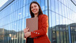 © PeopleVideos - Smiling businesswoman holding clipboard in front of modern office building