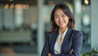 © f_bossa - A portrait headshot photo of a friendly professional CEO executive business worker: A smiling Asian businesswoman with short dark hair confidently poses with her arms crossed in a modern office l
