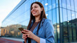 © PeopleVideos - Businesswoman smiling and using smartphone in front of modern office building