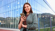 © PeopleVideos - Smiling businesswoman using smartphone in front of modern office building