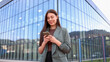 © PeopleVideos - Businesswoman using smartphone in front of modern office building