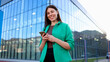 © PeopleVideos - Smiling businesswoman using smartphone in front of modern office building