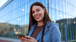 © PeopleVideos - Smiling businesswoman using smartphone in front of modern office building