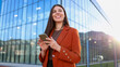 © PeopleVideos - Businesswoman using smartphone and smiling near office building at sunset