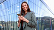 © PeopleVideos - Smiling businesswoman using smartphone in front of modern office building