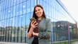 © PeopleVideos - Smiling businesswoman using smartphone in front of modern office building