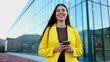 © PeopleVideos - Smiling businesswoman holding smartphone walking near office building