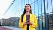© PeopleVideos - Smiling businesswoman holding smartphone standing near office building