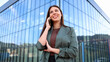 © PeopleVideos - Businesswoman smiling while talking on phone in front of modern office building