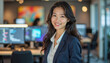 © f_bossa - A portrait headshot photo of a friendly professional CEO executive business worker: A smiling Asian woman in professional attire confidently poses in a modern office environment with computer scr