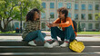 © Yuliia - Two happy African American friendly students conversation sitting outdoor multiracial friends African American woman girl female with boy man guy in city talking smiling university college high school
