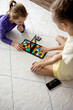 © evgeniia_1010 - Two children are focused on a colorful strategy game on a soft rug. One child uses a hand to move pieces while the other observes intently, creating a playful atmosphere at home