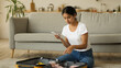 © Yuliia - Indian woman Arabian packing cloth with telephone check checklist with cellphone concentrated female girl at home preparing to trip vacation travel checking things list with mobile phone planning