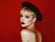 © Kien - an attractive blonde woman with short hair, wearing black lipstick and a hat, posing against a vibrant red background
