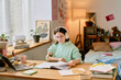 © AnnaStills - Girl with prosthetic hand studying at desk with headphones and open books in cozy room with various personal items placed around