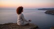 © Таня Андреева - A young woman (age 28) with curly red hair and dark skin sits in lotus position at the edge of a breathtaking cliff, overlooking a vast ocean