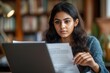 © wang - Serious Indian student working on research paper in library, reading essay, document. Focused young business woman reading investment agreement terms at laptop, financial reviewing reports