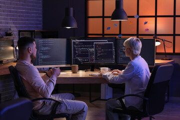 Wall Mural - young programmers working in office at night, back view