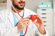 © Pixel-Shot - Young happy male doctor with stethoscope and red heart in clinic, closeup. World Health Day