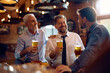 © Drazen - Happy male colleagues talking while drinking beer in pub after business meeting.