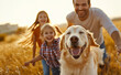 © Curioso.Photography - A happy family with two children and a golden retriever dog running together in a field during sunset.