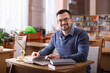 © New Africa - Portrait of smiling man with books at desk in library