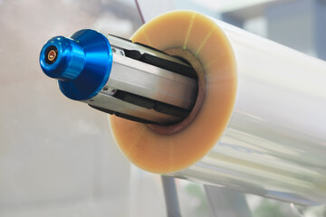 Poster - A machine with a roll of polyethylene plastic film on it. The machine is in a factory. industrial food packaging concept background